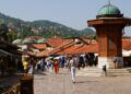 " view of Sarajevo skyline with historic Baščaršija district in the foreground and surrounding Dinaric Alps under a clear blue sky."