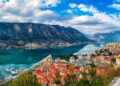 The Bay of Kotor in Montenegro at sunset, a UNESCO World Heritage Site, showcases dramatic mountains, tranquil waters, and historic towns bathed in golden light.