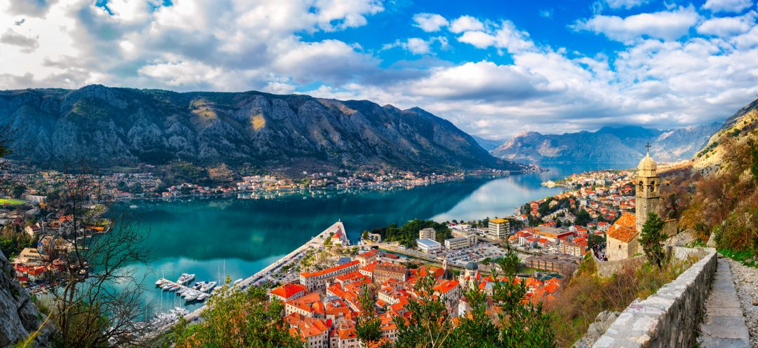The Bay of Kotor in Montenegro at sunset, a UNESCO World Heritage Site, showcases dramatic mountains, tranquil waters, and historic towns bathed in golden light.