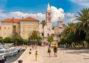 Brac Island, Croatia — Scenic view of Supetar's historic waterfront with people strolling, palm trees, and boats on Brac Island.