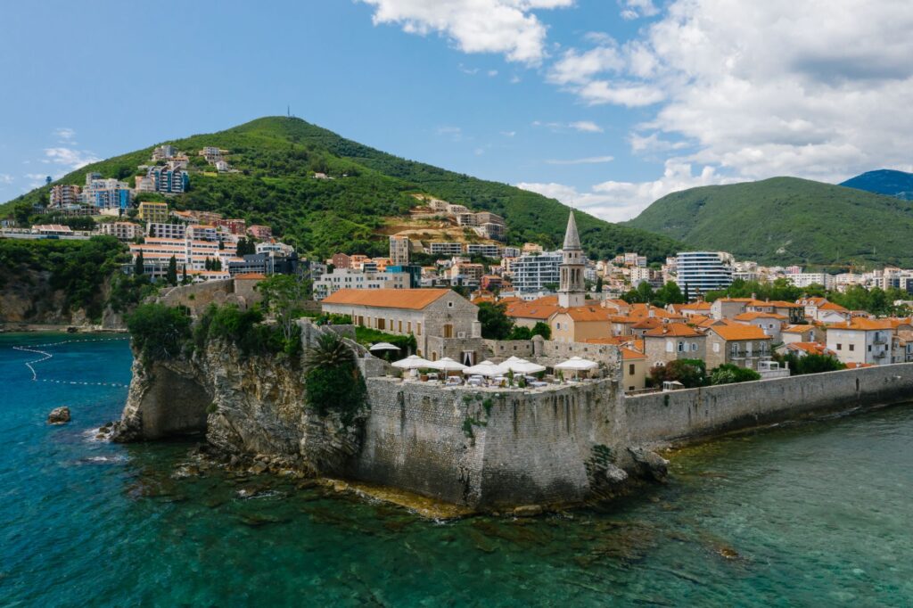 Budva, Montenegro — Aerial view of a historic town on the Adriatic coast, featuring old stone walls and lush green mountains.