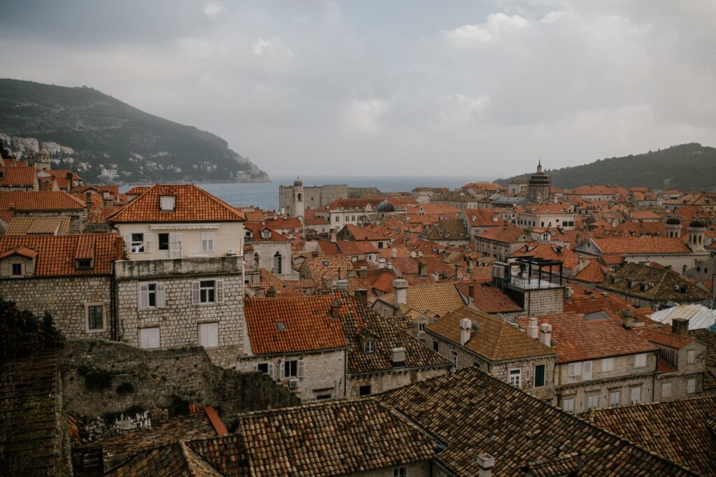 Dubrovnik, Croatia — Cityscape of residential houses with tiled roofs and brick walls on hills near calm ocean in overcast weather