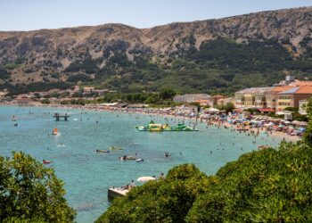 Krk Island, Croatia — Lively summer beach scene in Baška, Croatia with mountains and clear waters.