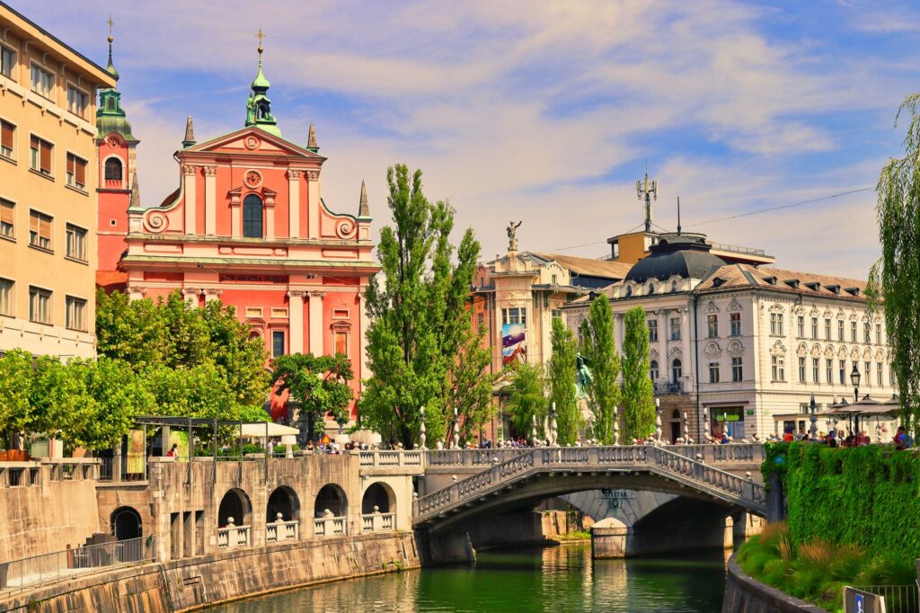 Ljubljana, Slovenia — Explore Ljubljana's vibrant cityscape with the Triple Bridge and Franciscan Church on a sunny day.