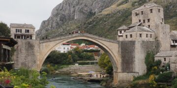 Mostar, Bosnia and Herzegovina — Scenic view of the historic Stari Most Bridge over the Neretva River in Mostar, surrounded by hills and buildings.