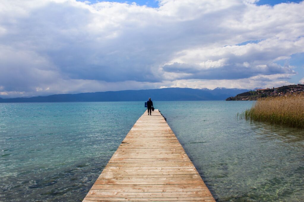 Ohrid, North Macedonia — A serene view of a wooden pier extending into Lake Ohrid under a bright sky in North Macedonia.