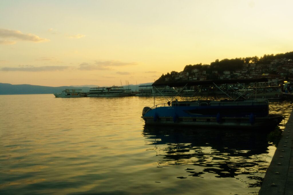 Ohrid, North Macedonia — Peaceful sunset view at Ohrid Lake featuring boats and distant hills under a warm glow.