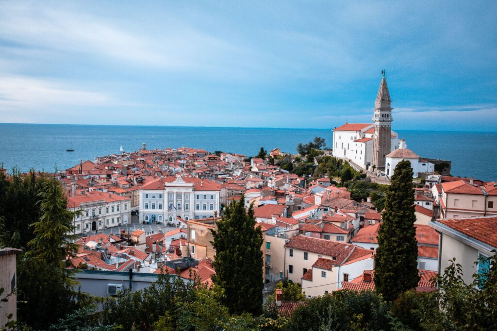 Piran, Slovenia — Scenic view of a coastal town featuring historic buildings and church by the sea.