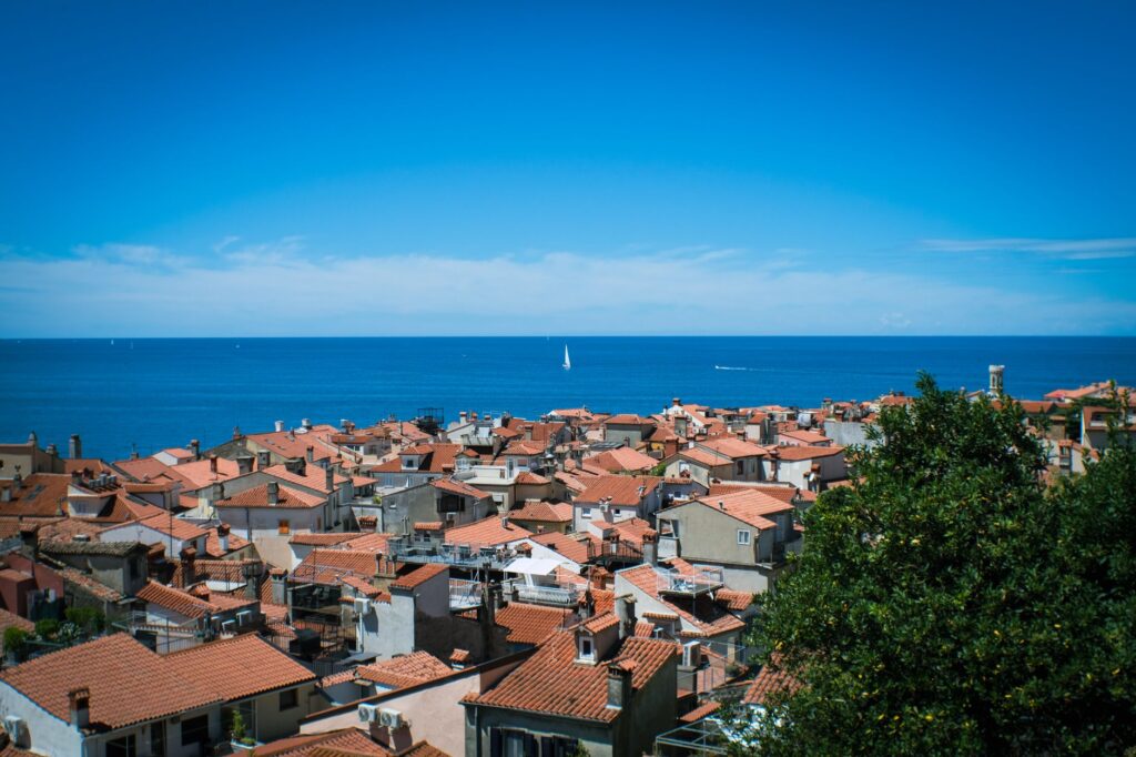 Piran, Slovenia — A picturesque view of Piran's terracotta rooftops and the Adriatic Sea under a clear blue sky.