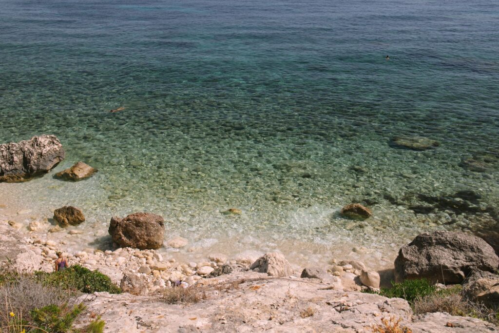 Saranda, Albania — A tranquil rocky beach with clear turquoise waters under the summer sun, perfect for travel and relaxation.