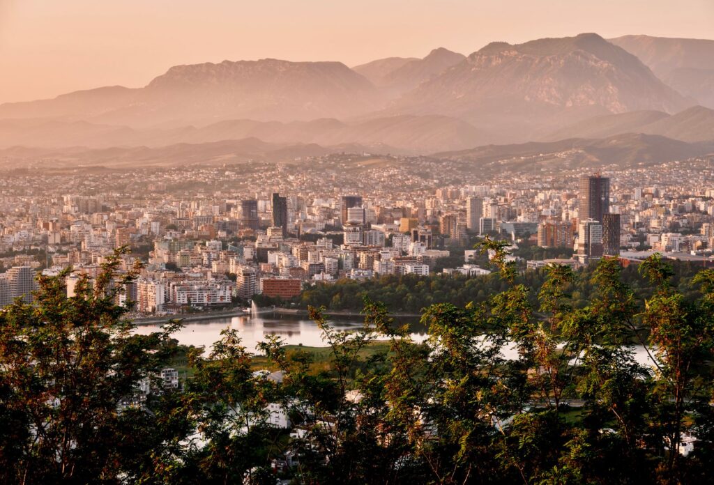 Tirana, Albania — A stunning aerial view of Tirana's skyline framed by mountains and lush greenery during sunset.