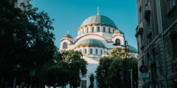 Belgrade, Serbia — View of the iconic Saint Sava Temple in Belgrade on a sunny day, framed by trees and buildings.