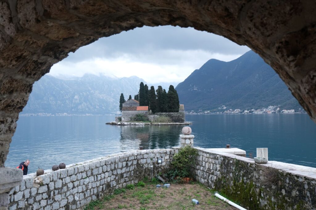 Kotor, Montenegro — Serene island view framed by stone arch in Kotor Bay, Montenegro.