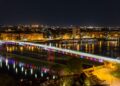 Novi Sad, Serbia — Night view of the illuminated bridge over the Danube River in Novi Sad, showing vibrant reflections and cityscape.