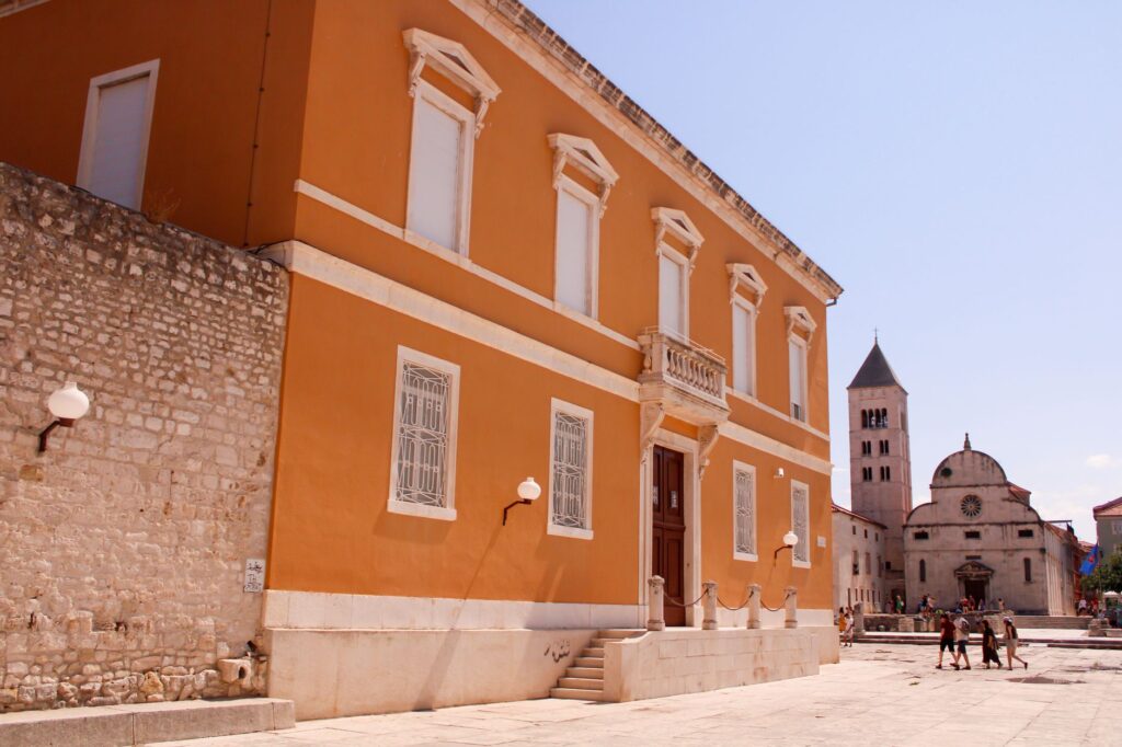 Zadar, Croatia — Explore the charming orange facade of a historic building in Zadar with a tower in the background.