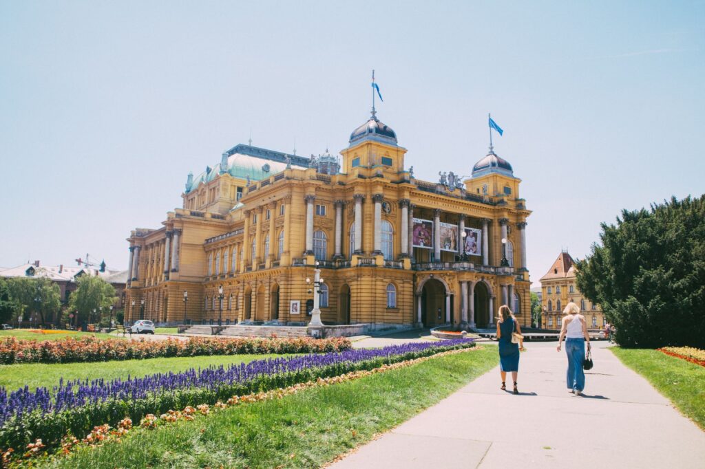 Zagreb, Croatia — A sunny day view of the Croatian National Theatre with flowerbeds and people walking.