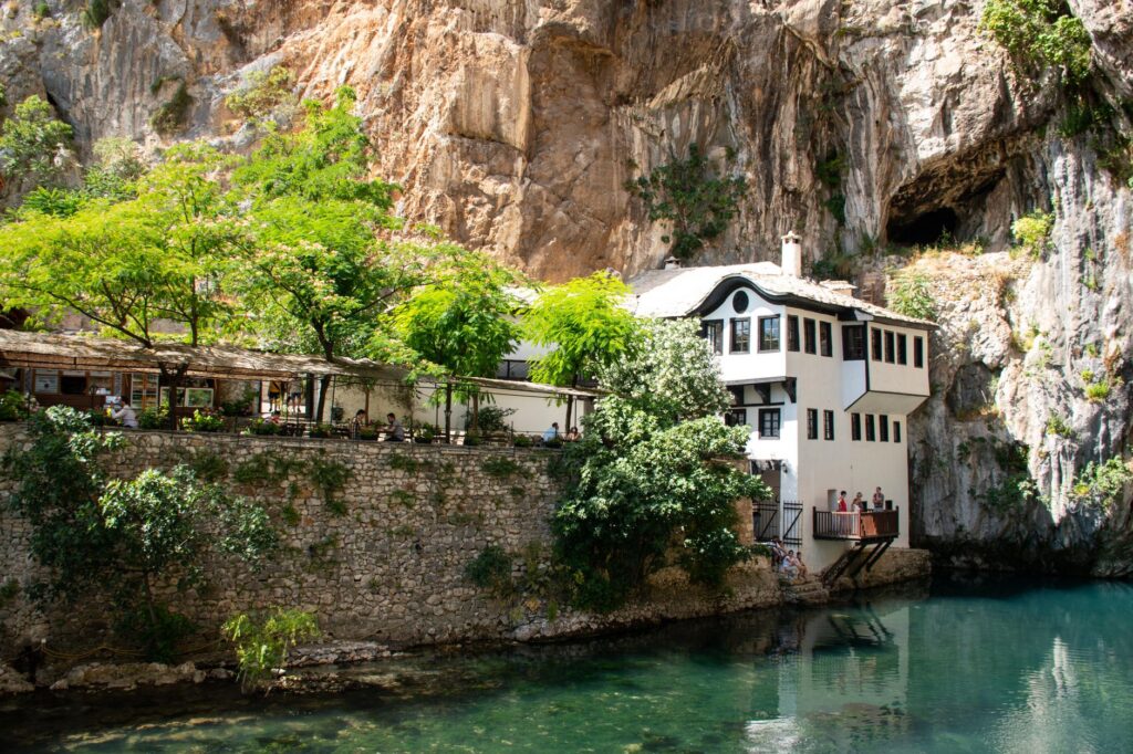 Blagaj, Bosnia and Herzegovina — Scenic view of Blagaj Tekke alongside the Buna River, framed by cliffs and lush trees.