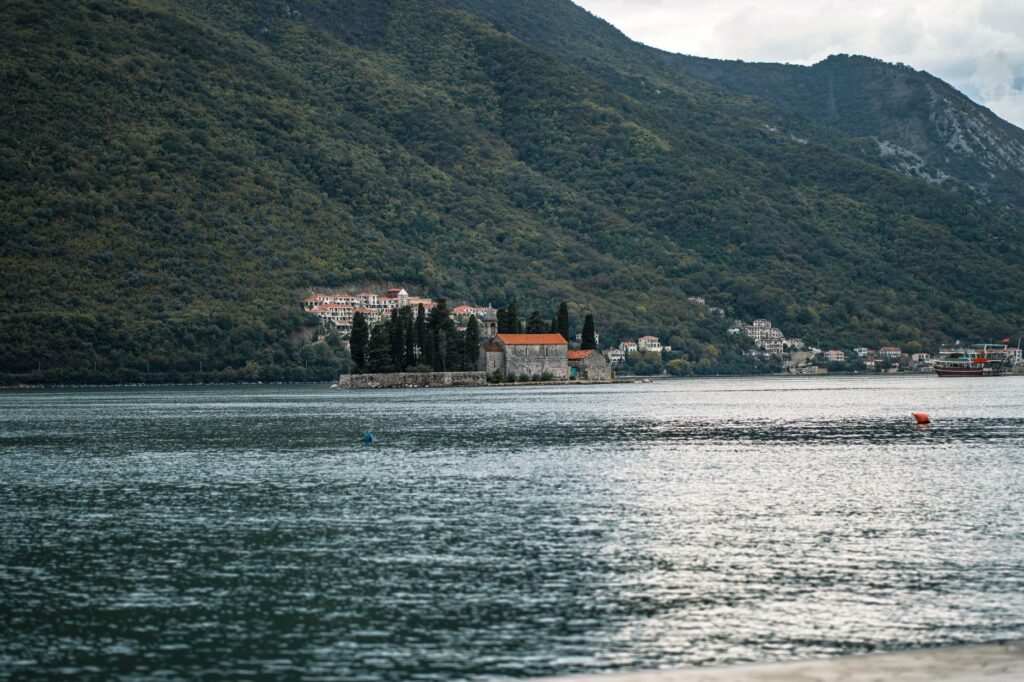 Perast, Montenegro — Peaceful lake view of Perast Island surrounded by lush mountains, perfect for travel and nature enthusiasts.