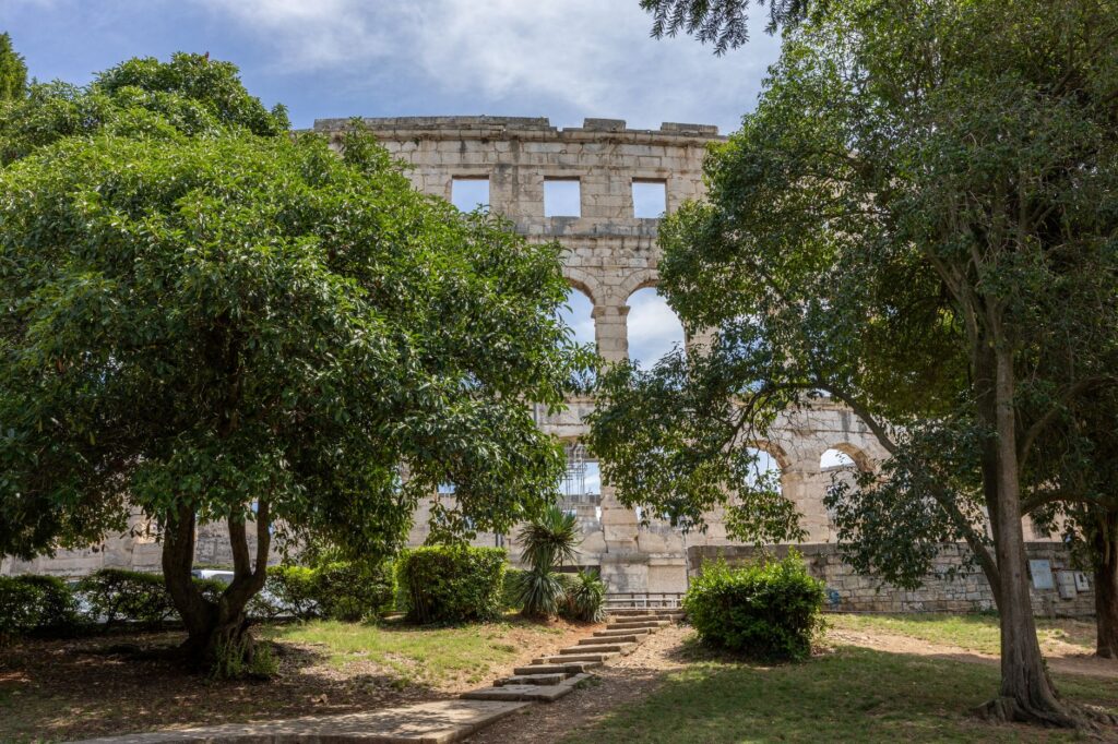 Pula, Croatia — A serene view of the ancient Roman amphitheater in Pula, Croatia, framed by lush green trees.