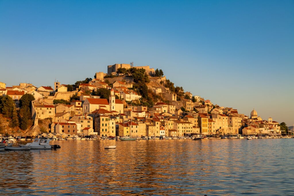 Šibenik, Croatia — A picturesque view of Šibenik's historic waterfront at sunset, reflecting golden hues.