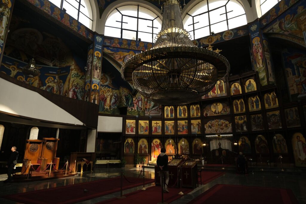 Skopje, North Macedonia — The ornate interior of St. Clement of Ohrid Church in Skopje, showcasing vibrant religious frescoes and a grand chandelier.