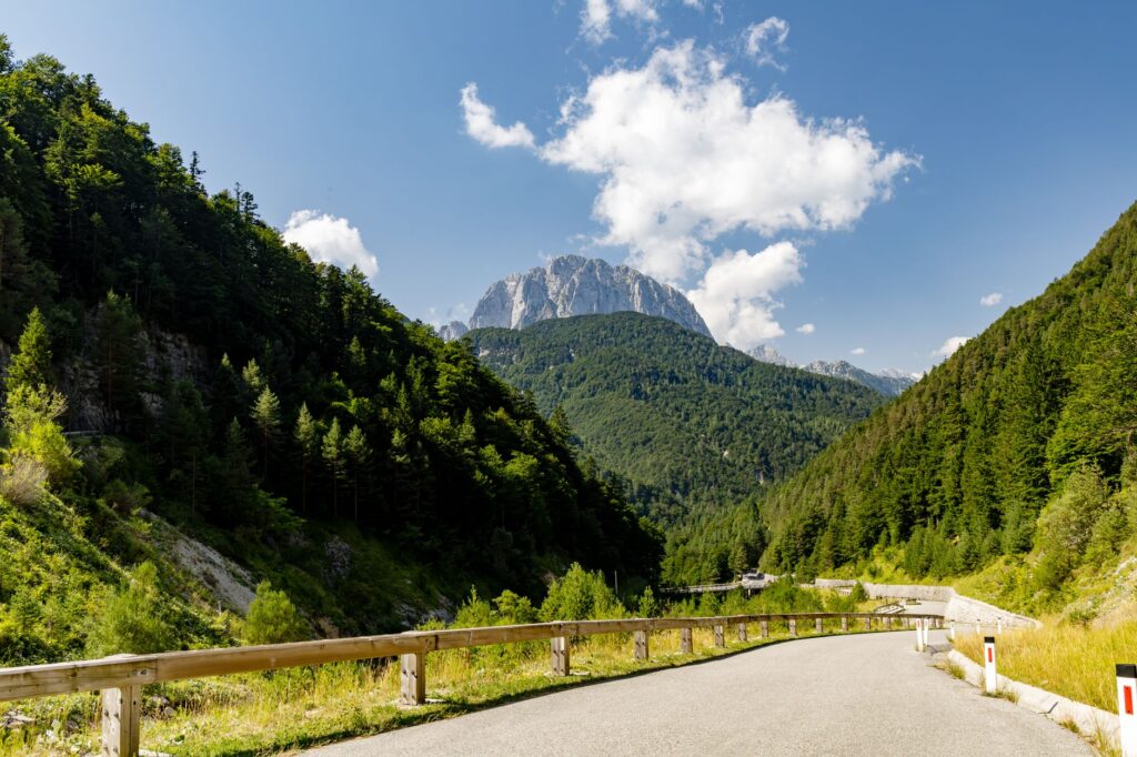 Soča Valley, Slovenia — A panoramic view of a winding road through lush green forests and the majestic Julian Alps under a clear blue sky.